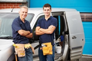Two tradespeople smiling beside their work van